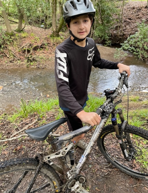 Rocco, a young Climate Rider in a Fox shirt standing beside his muddy mountain bike.